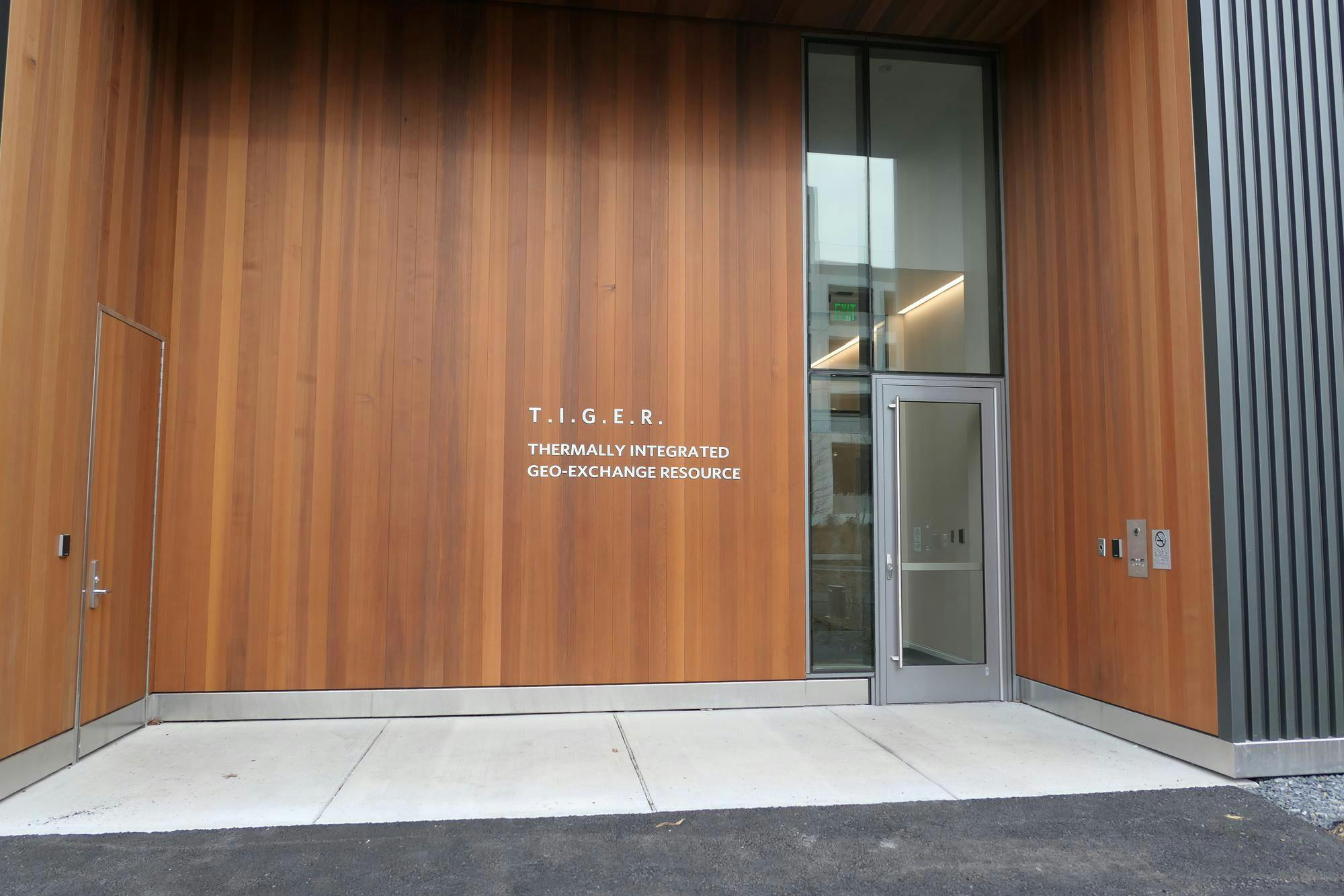 A glass door surrounded by wood panelling printed with the words “T.I.G.E.R.” and “Thermally Integrated Geo-Exchange Resource” in bold white lettering. 