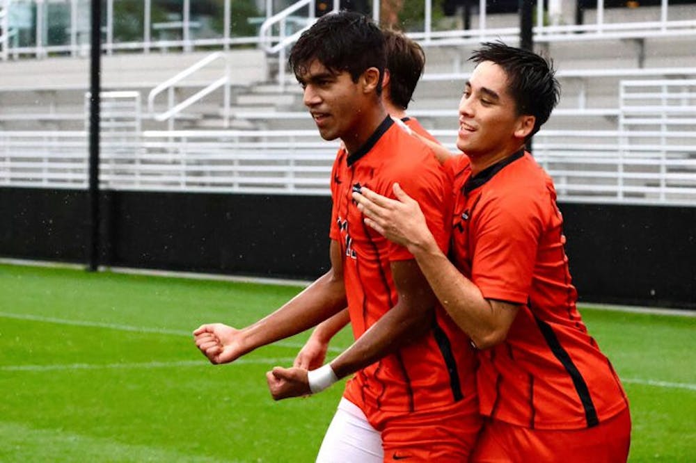 Three soccer players wearing orange jerseys with black stripes cheer on the field.