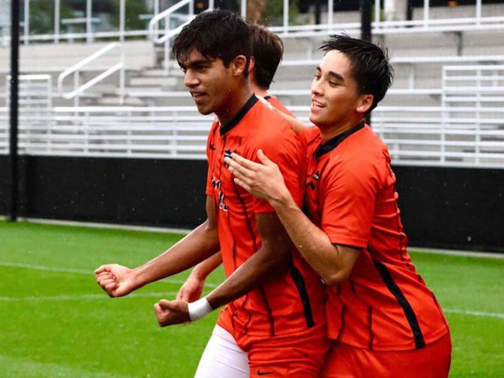 Three soccer players wearing orange jerseys with black stripes cheer on the field.