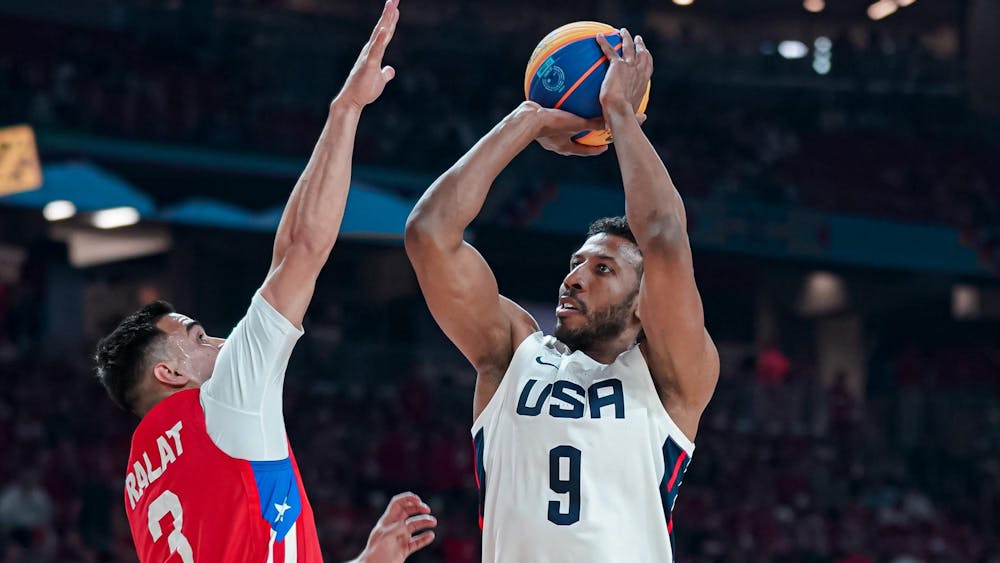 A man in a red, white, and blue USA jersey prepares to shoot an orange and blue basketball.