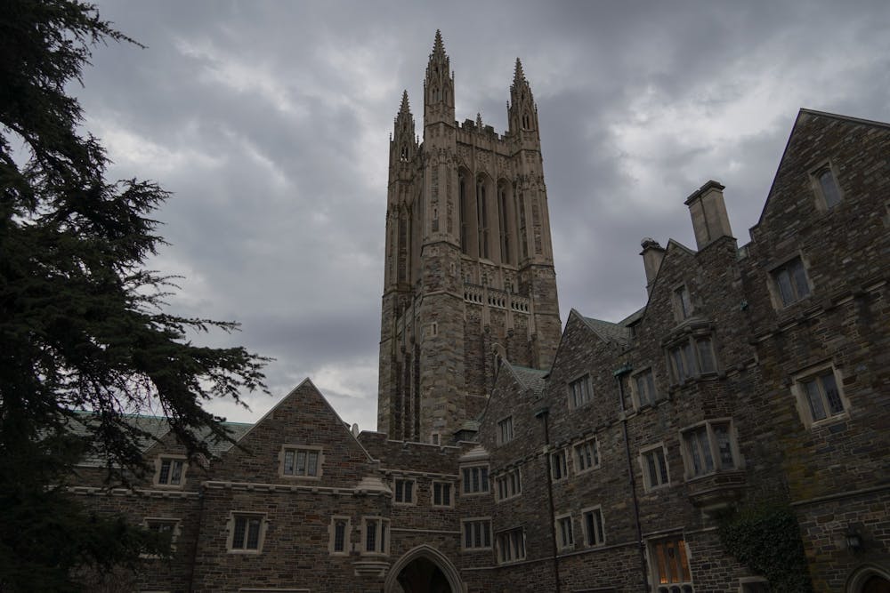 Photo of a gothic stone tower above other stone buildings against a cloudy gray sky.