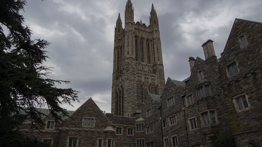 Photo of a gothic stone tower above other stone buildings against a cloudy gray sky.