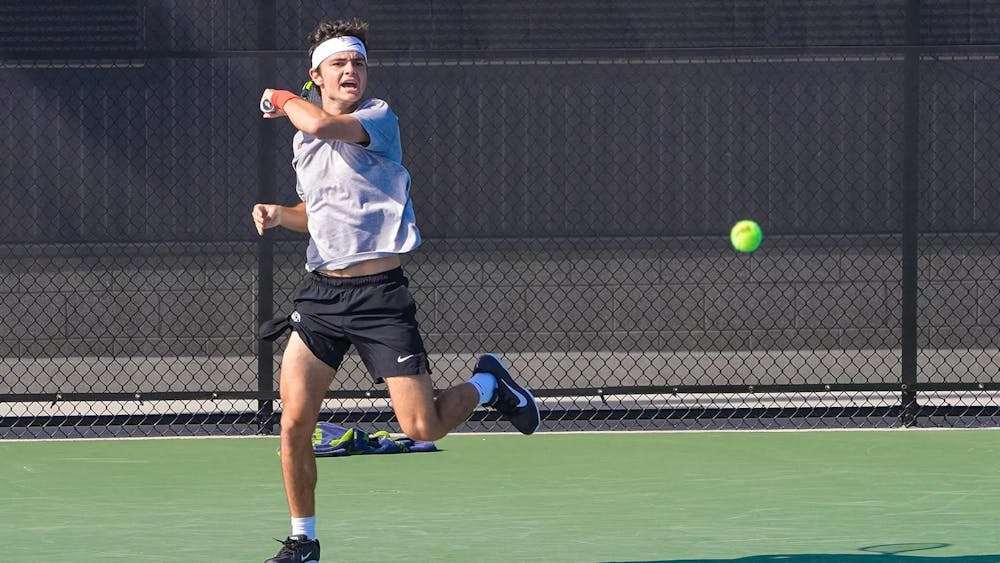 A tennis player in a white shirt and black shorts hits a tennis ball.