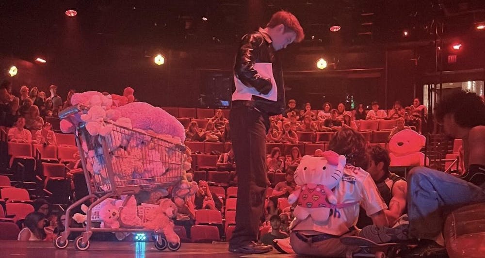 A man stands on stage next to a cart filled with stuffed animals.