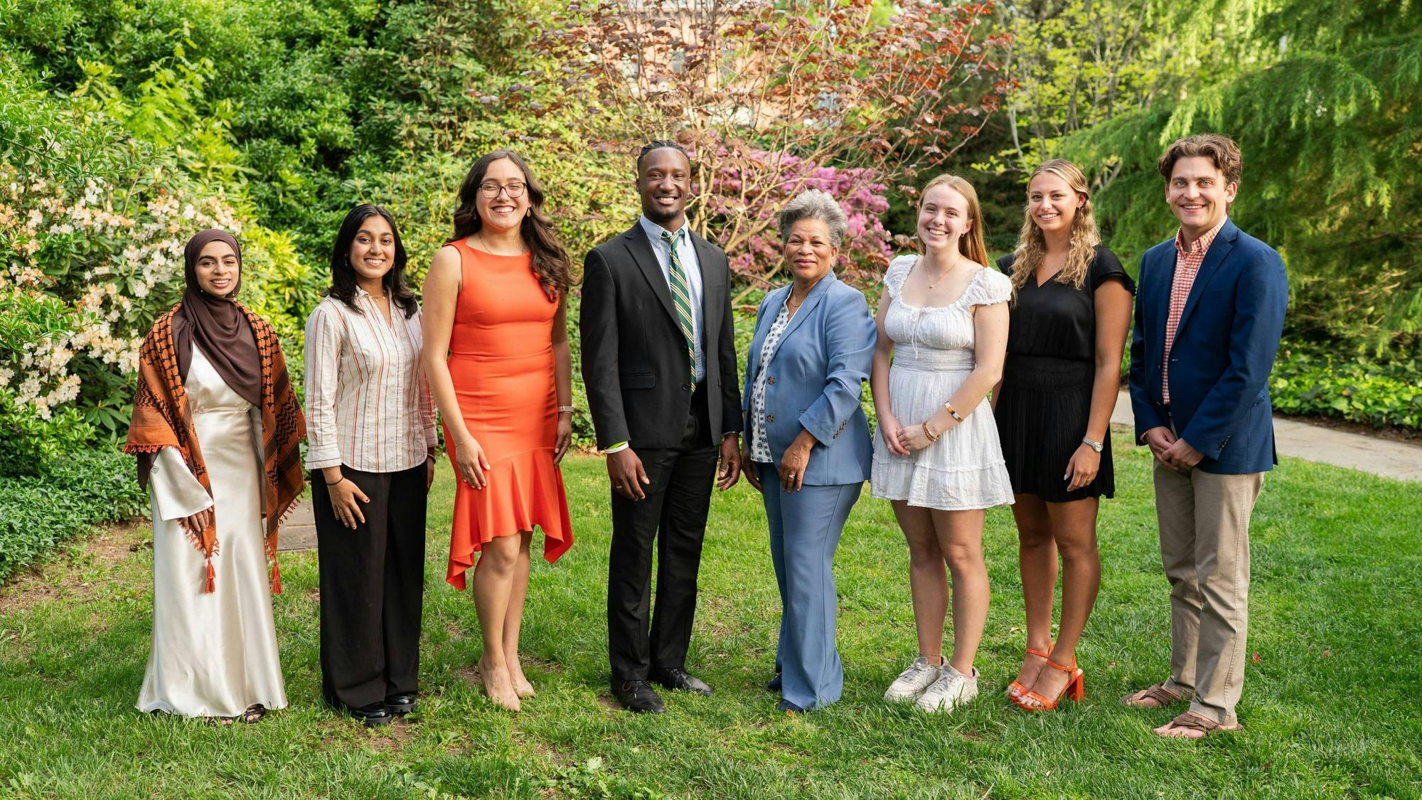 Eight people standing on grass, professionally dressed for a photo. 