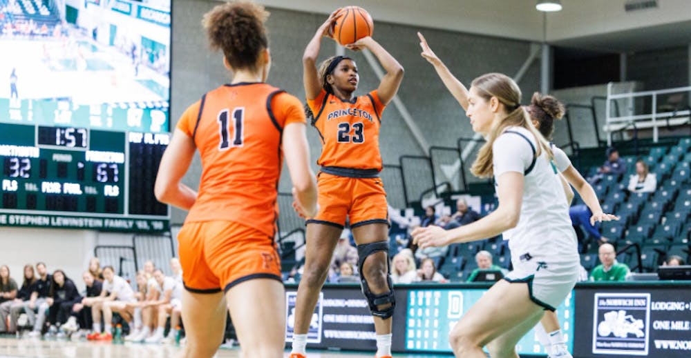 A player wearing an orange jersey is shooting midair over a player in a white jersey.
