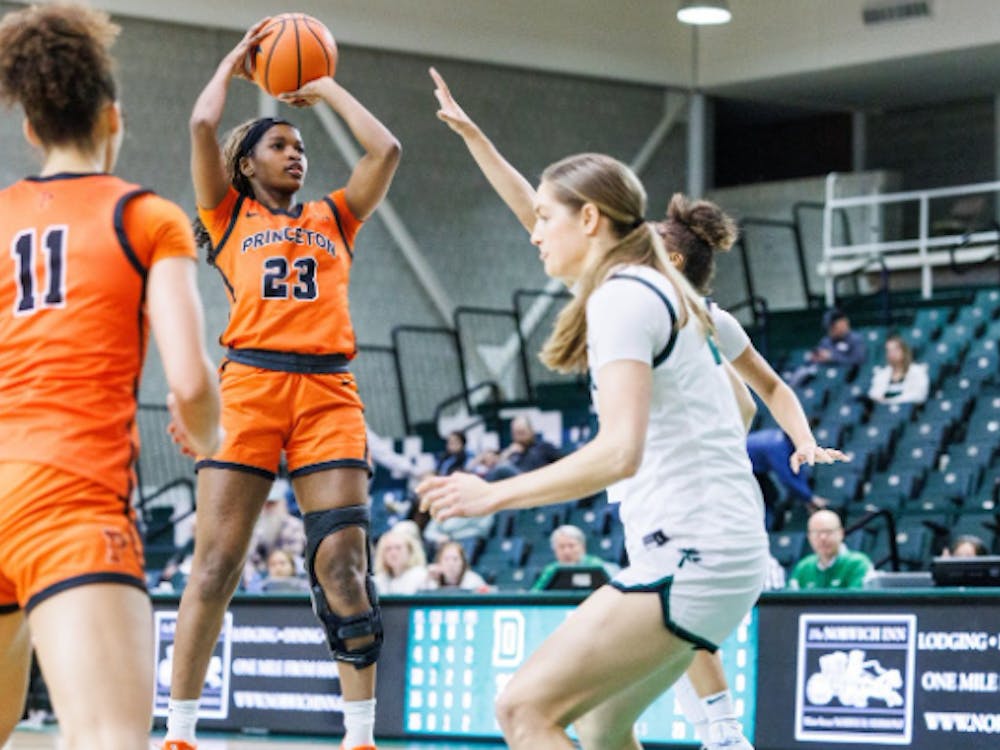 A player wearing an orange jersey is shooting midair over a player in a white jersey.