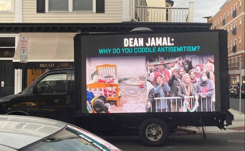 A truck with a screen reading "DEAN JAMAL: WHY DO YOU CODDLE ANTISEMITISM” and with images of a bed with bloodied sheets and a group of protesters holding Palestinian flags. 