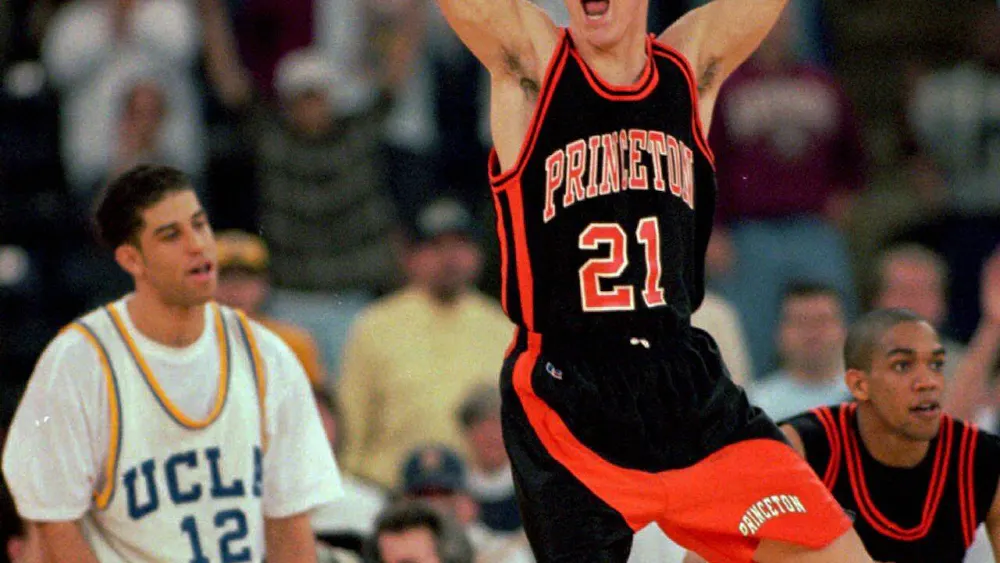 Photograph of Princeton basketball player, Mitch Henderson ’98, in his uniform, jumping in the air with a UCLA basketball player and teammate Sydney Johnson ’97 behind him.