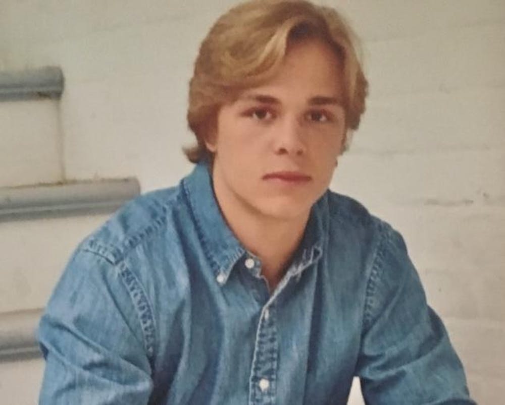 Tiger Bech, wearing a blue collared shirt, sits on a set of stairs with his arms on his legs while looking at the camera.