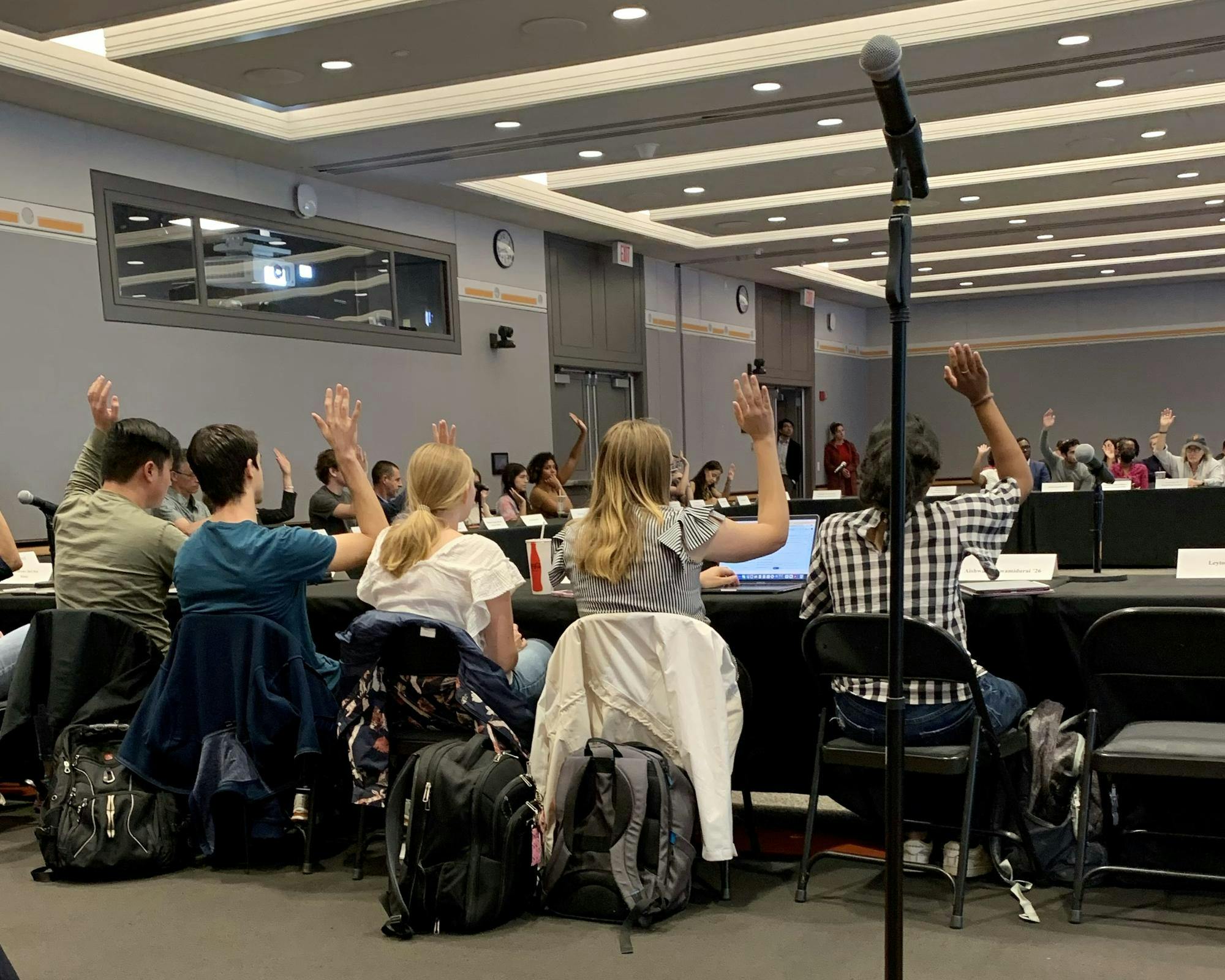 Five people, seated at a long table, raise their hands in a vote.