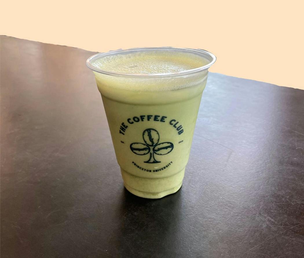 A cup of iced matcha sits on a table in front of a light orange background.