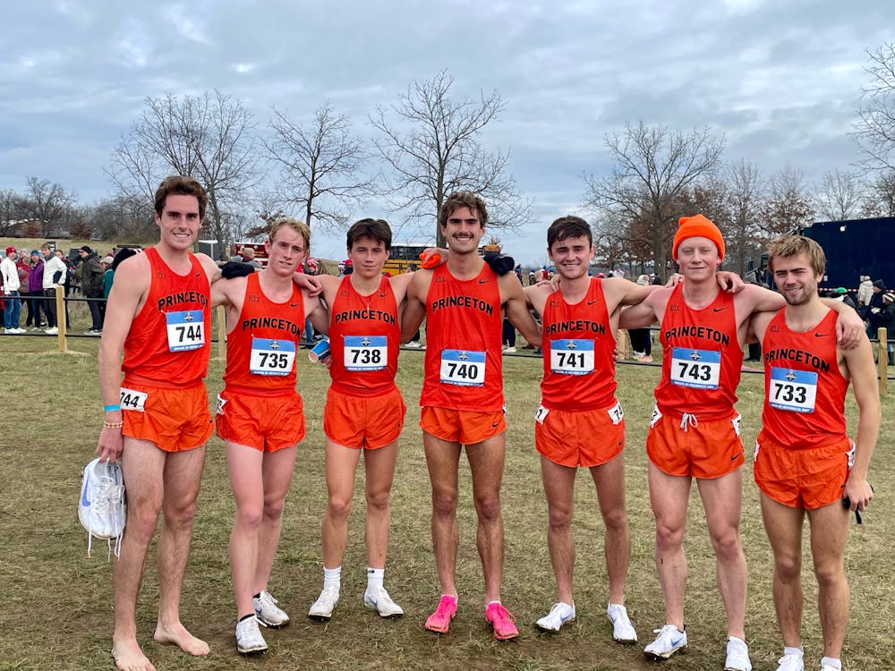 Seven men in orange with number labels pinned on pose together with big smiles. 