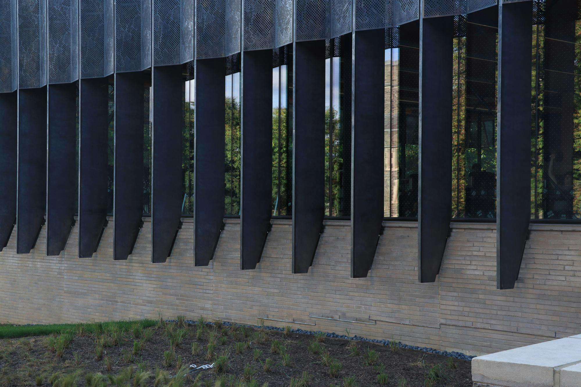 Many long glass windows, separated by black steel walls, atop a grey brick wall.