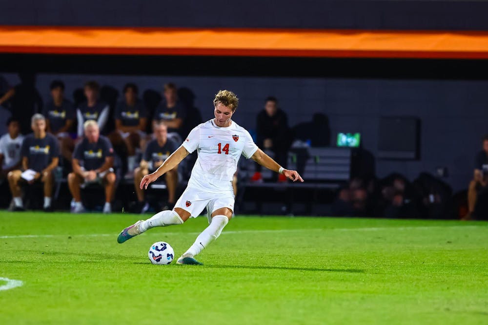 A man in a white jersey on a grass field getting ready to kick a soccer ball. 