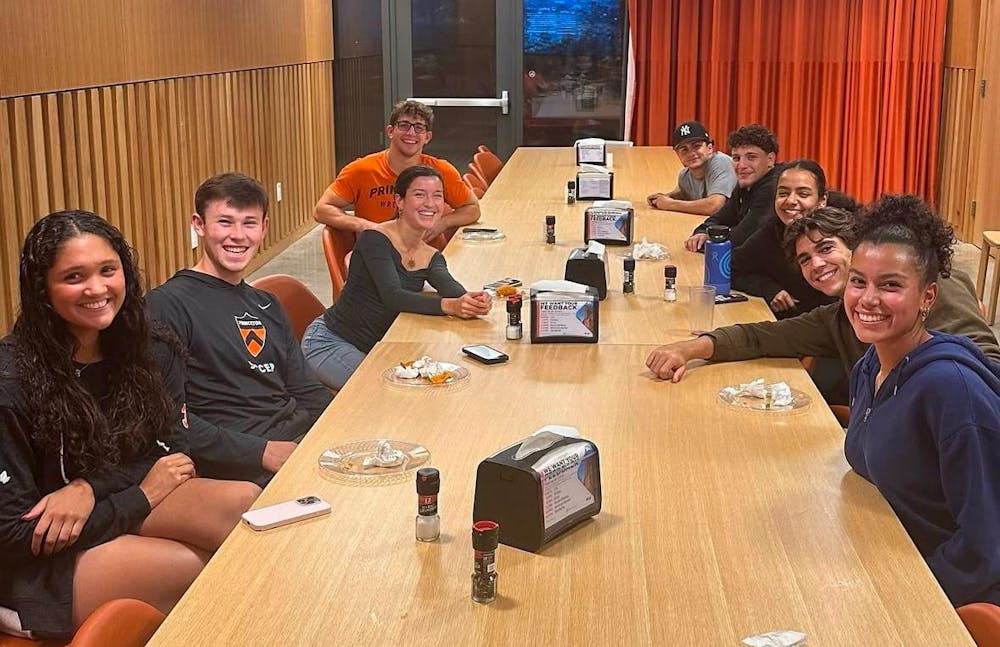 Students sit at a long wooden dining table.