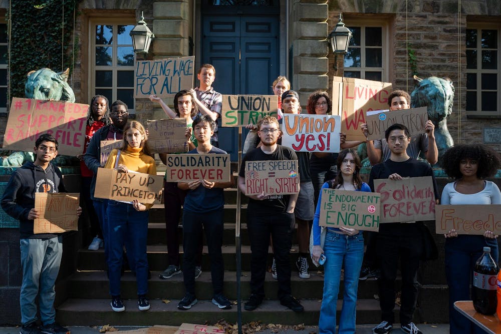 Students stand in front of stone building with signs that express union solidarity. 