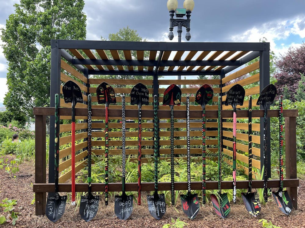 A collection of decorated shovels stand before a wooden enclosure with plants in the background at the Botanical Gardens in Washington, DC.