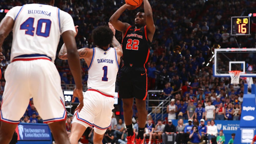A player in a black jersey jumping and shooting a basketball in front of a player in a white jersey.