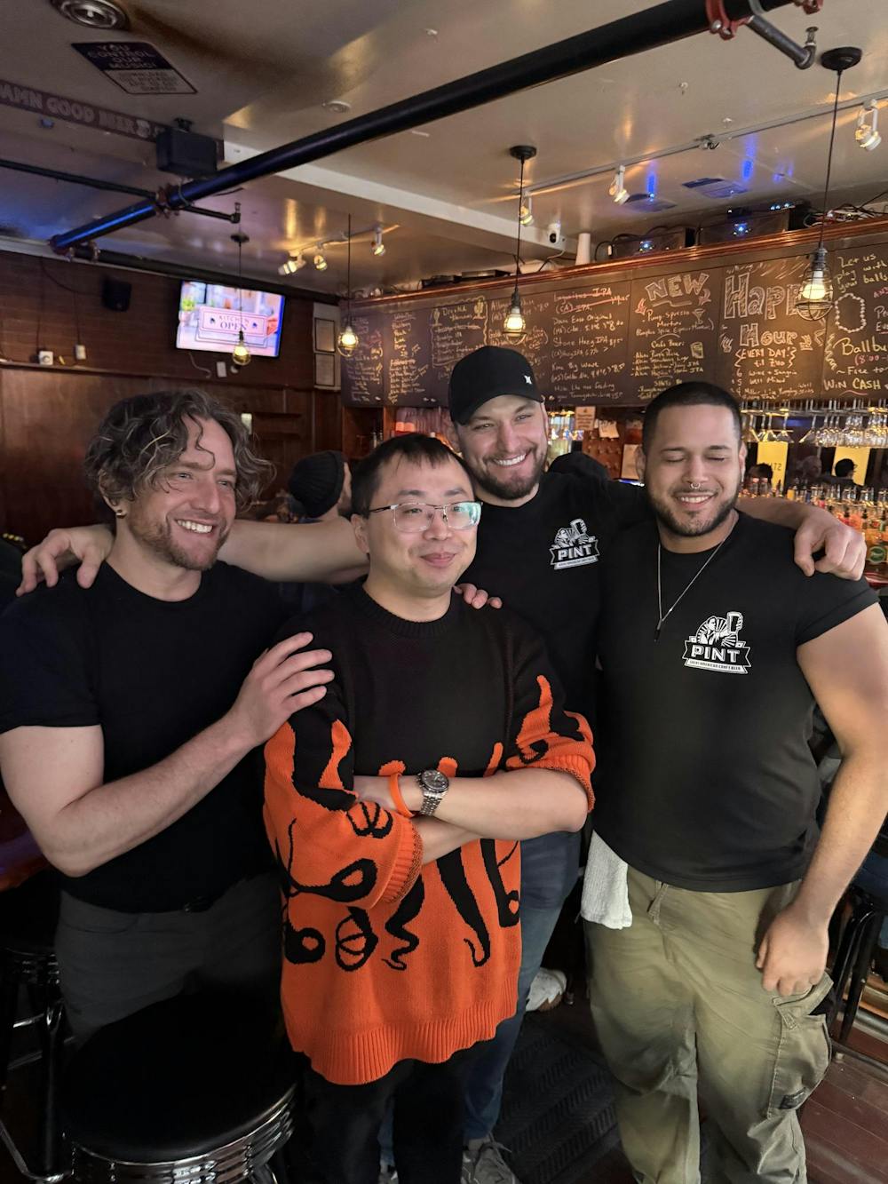 Four men stand at a bar. 