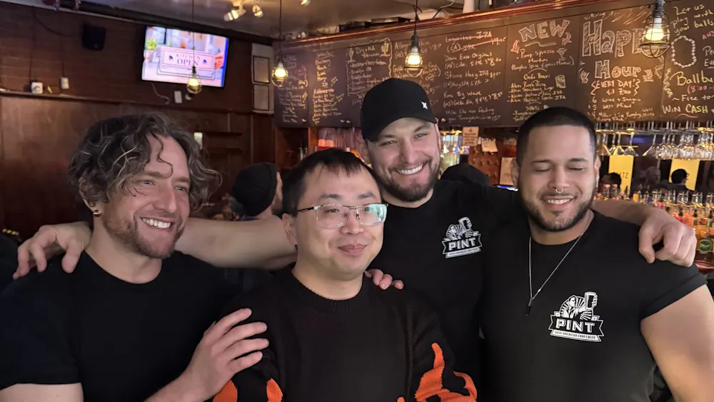 Four men stand at a bar.