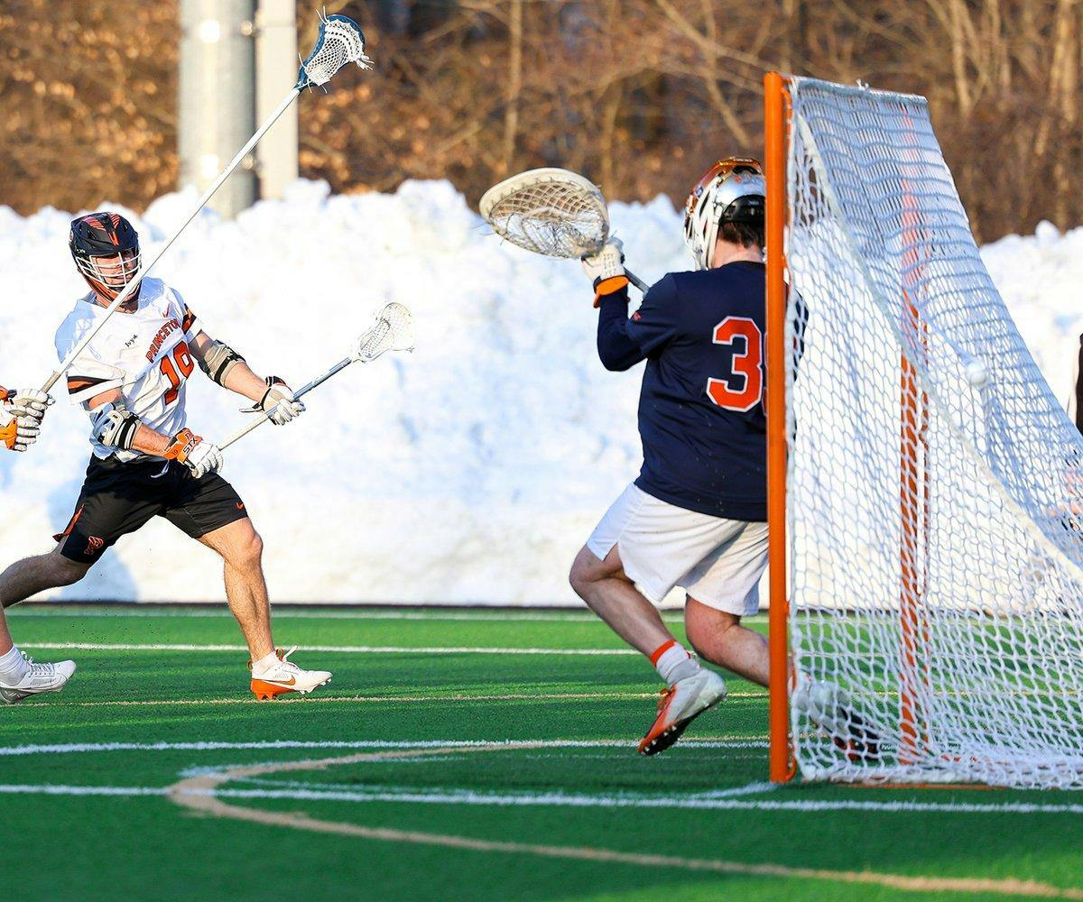 Princeton lacrosse player in white jersey shoots and scores against Syracuse goalie in navy and orange jersey.