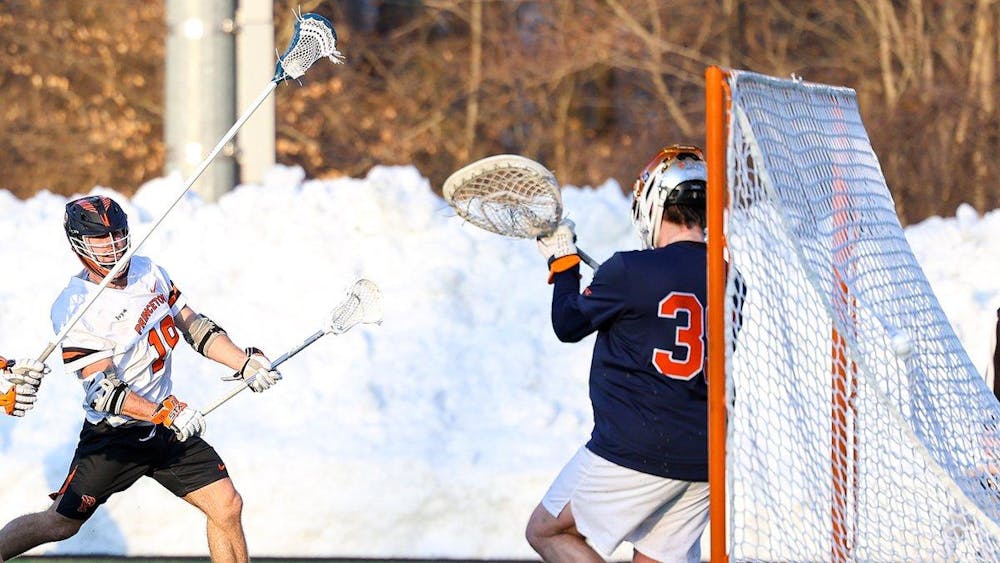 Princeton lacrosse player in white jersey shoots and scores against Syracuse goalie in navy and orange jersey.