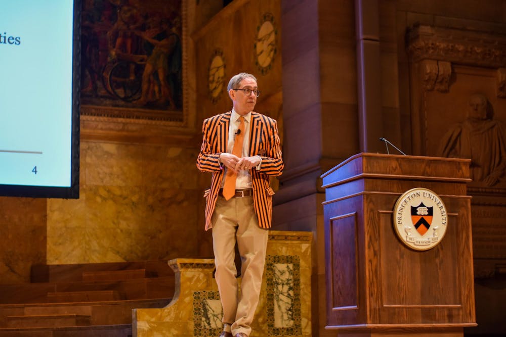 A man in a black and orange striped blazer and orange tie stands next to a podium adorned with a Princeton University crest.