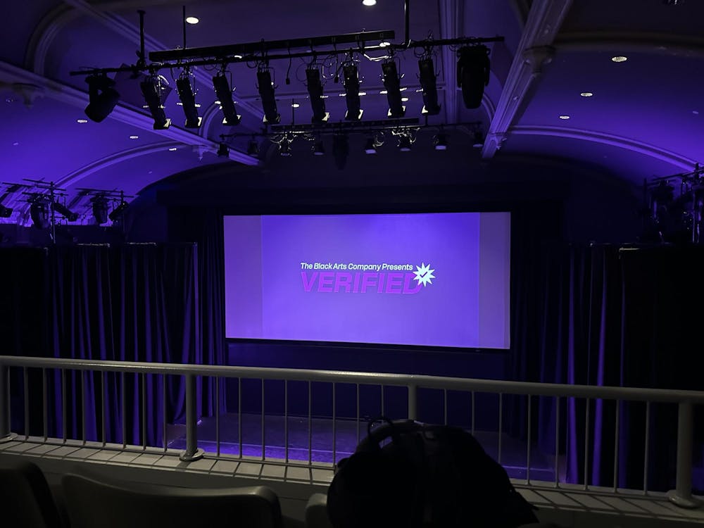 An image of the Black Arts Company's title screen for their show. It says "Black Arts Company: Verified" in white and purple lettering. The lighting in Frist Theater is purple.