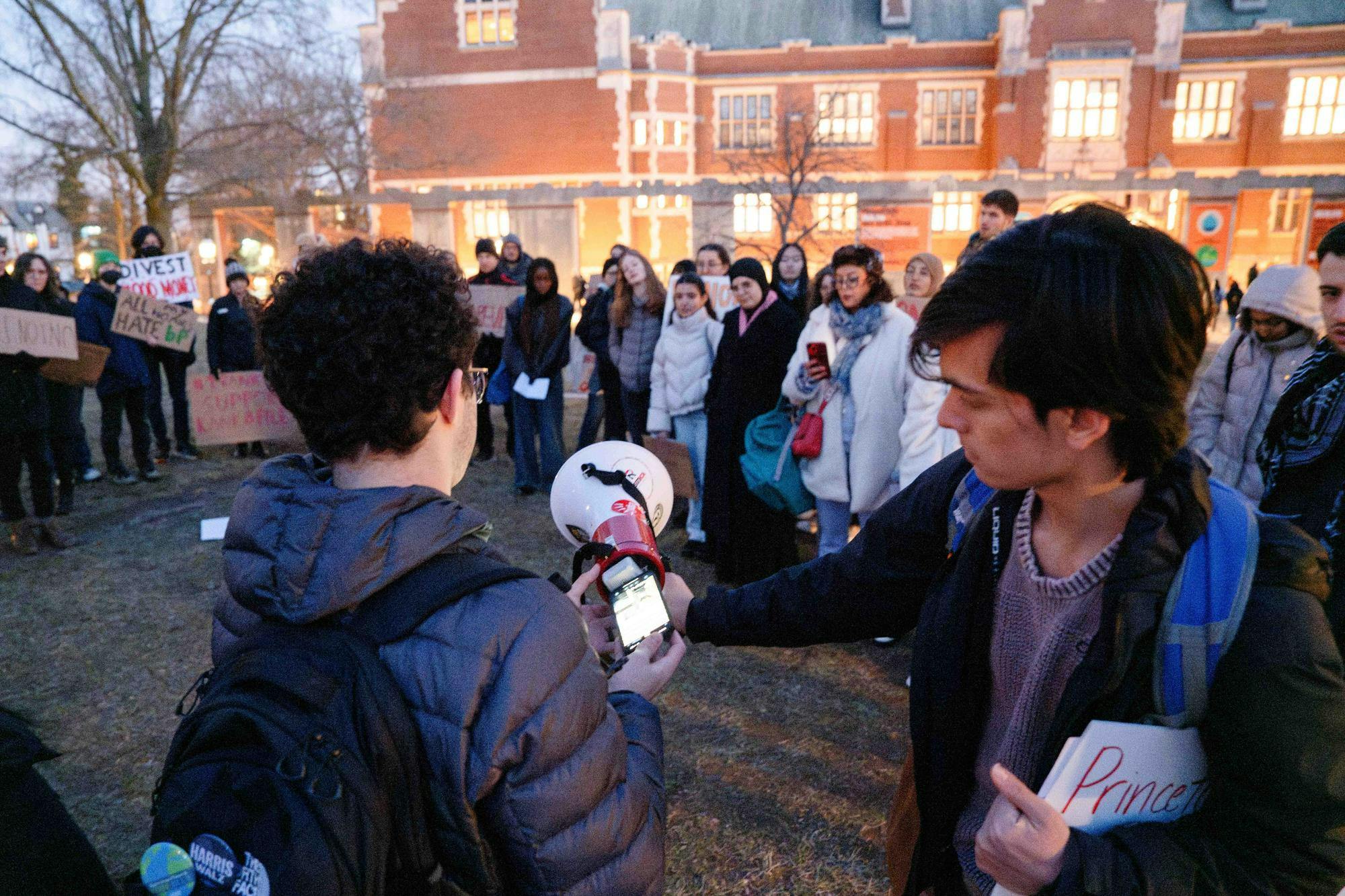 two people hold up a cell phone to a megaphone in front of a crowd 