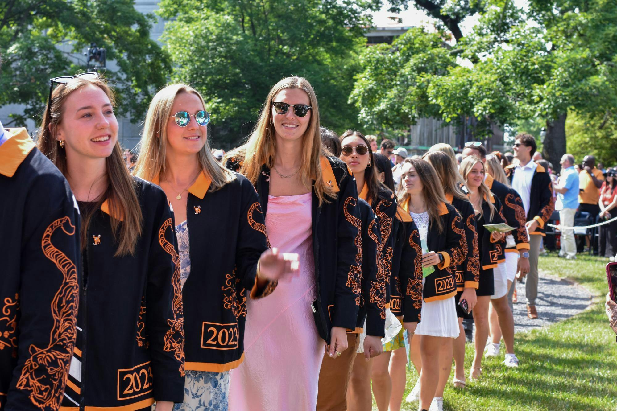 A group of people wearing an orange and black custom jacket while walking on grass.