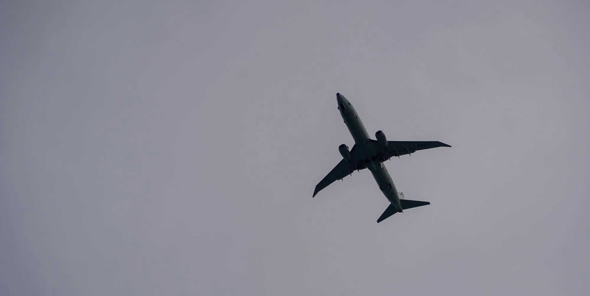 A white commercial airplane flies overhead on an overcast day. 