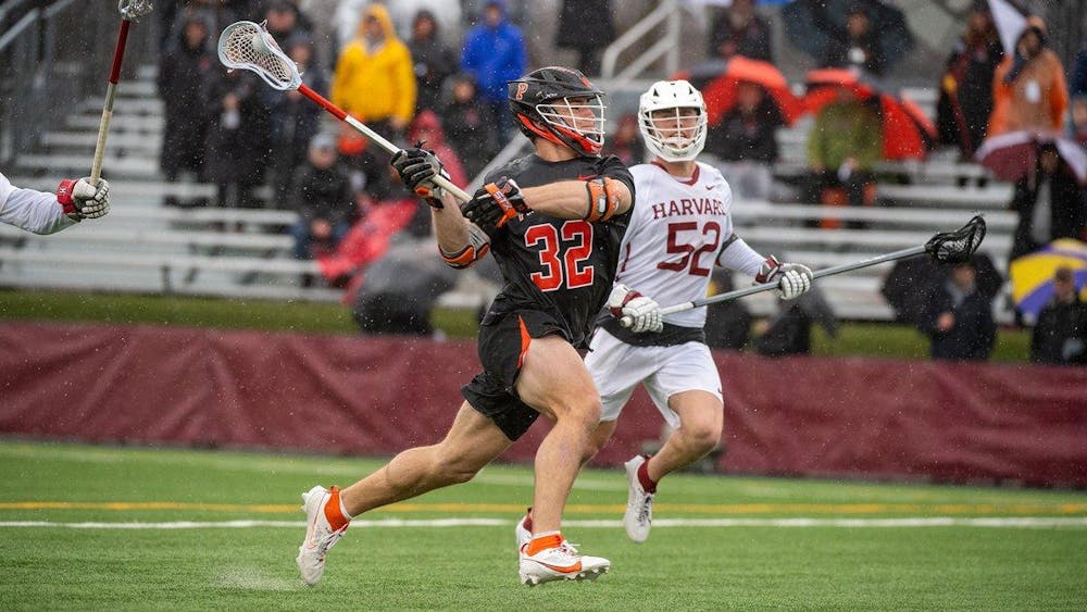 Lacrosse player in orange and black runs with ball in stick, with heavy rain coming down and a lacrosse player from the opposing team chasing.