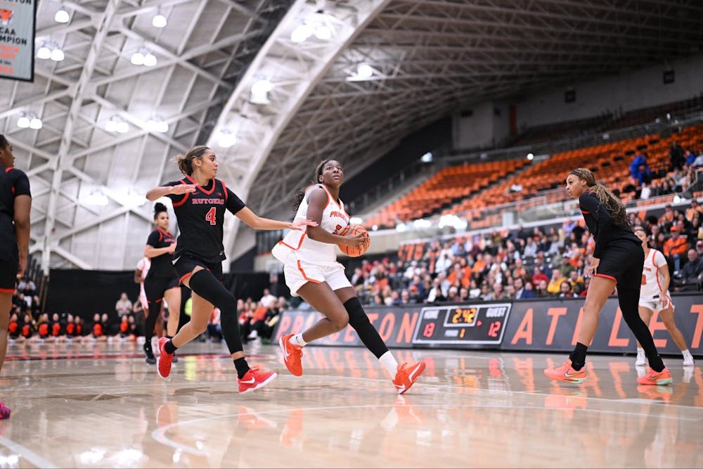 A woman in a white and orange jersey shoots a layup while another player in a black jersey tries to stop her.