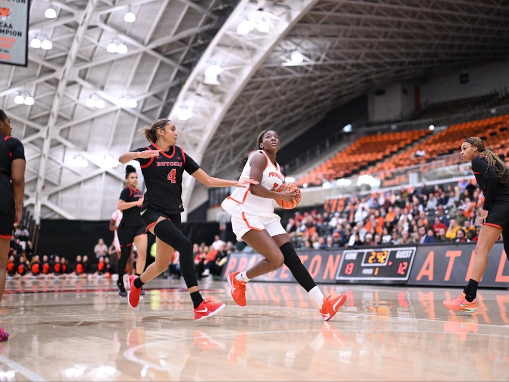 A woman in a white and orange jersey shoots a layup while another player in a black jersey tries to stop her.