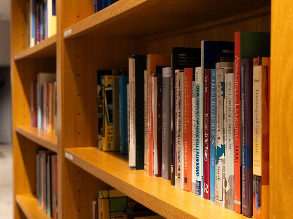 Mostly orange and blue books sit on a shelf. 