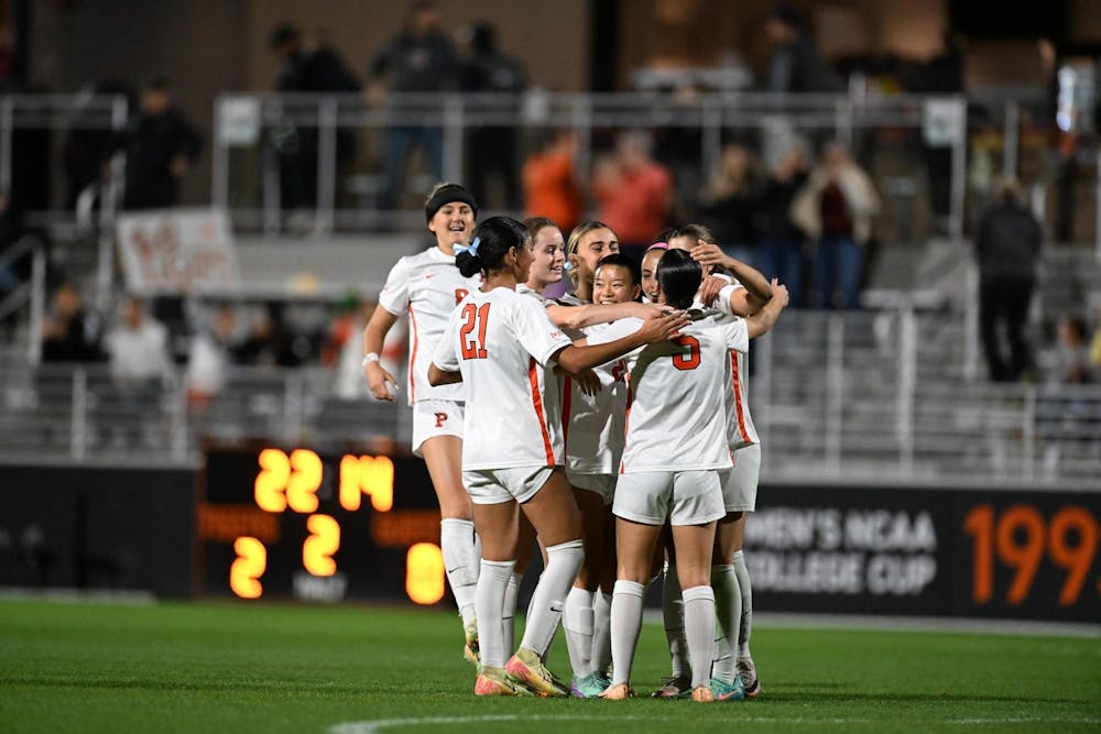 A group of woman wearing white jerseys and shorts embrace together after scoring a goal. 