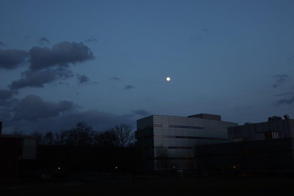 There is a building with trees around it. In the background, the sky is dark and the moon hangs low in the sky.