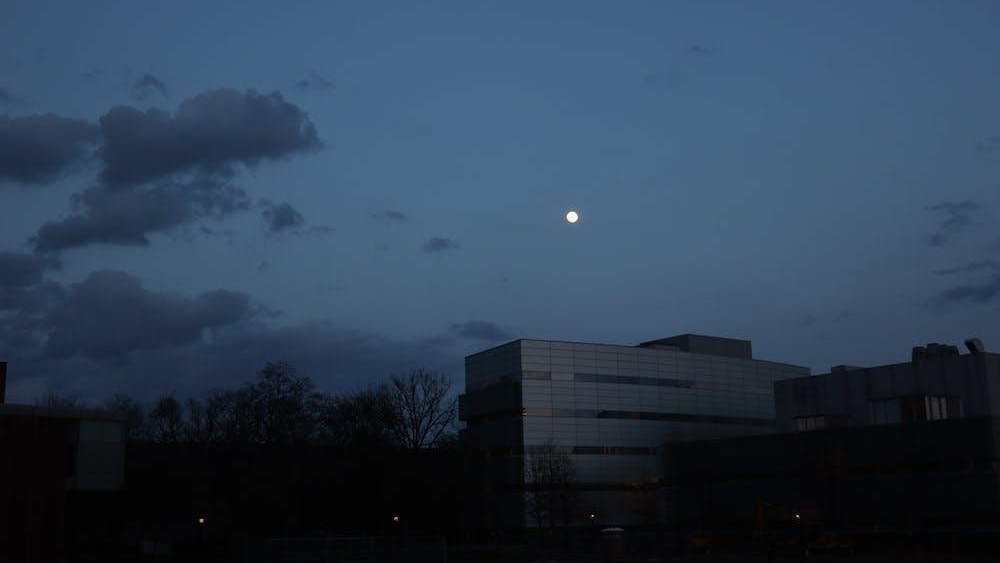 There is a building with trees around it. In the background, the sky is dark and the moon hangs low in the sky.