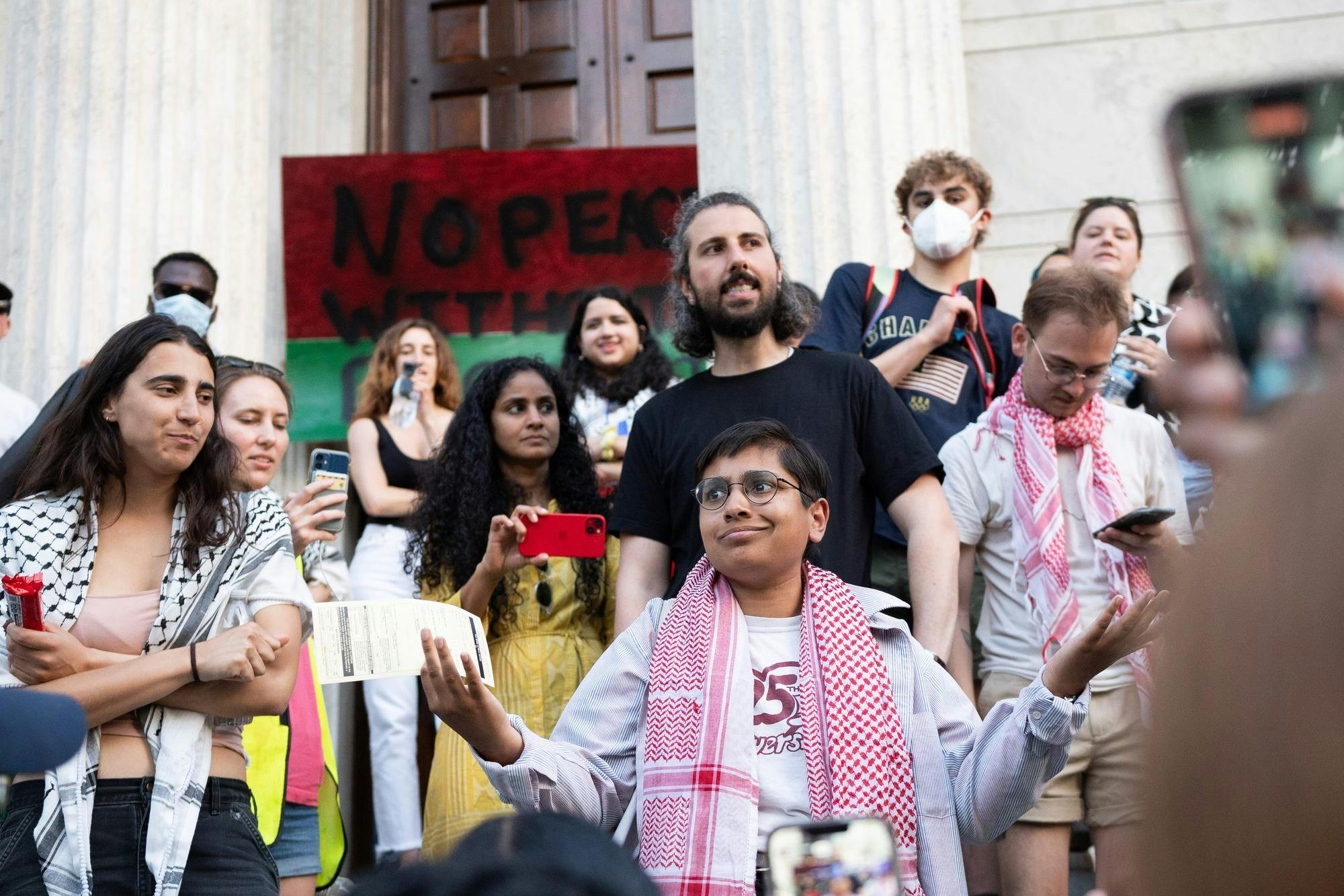 A speaker faces a crowd while shrugging defiantly. 