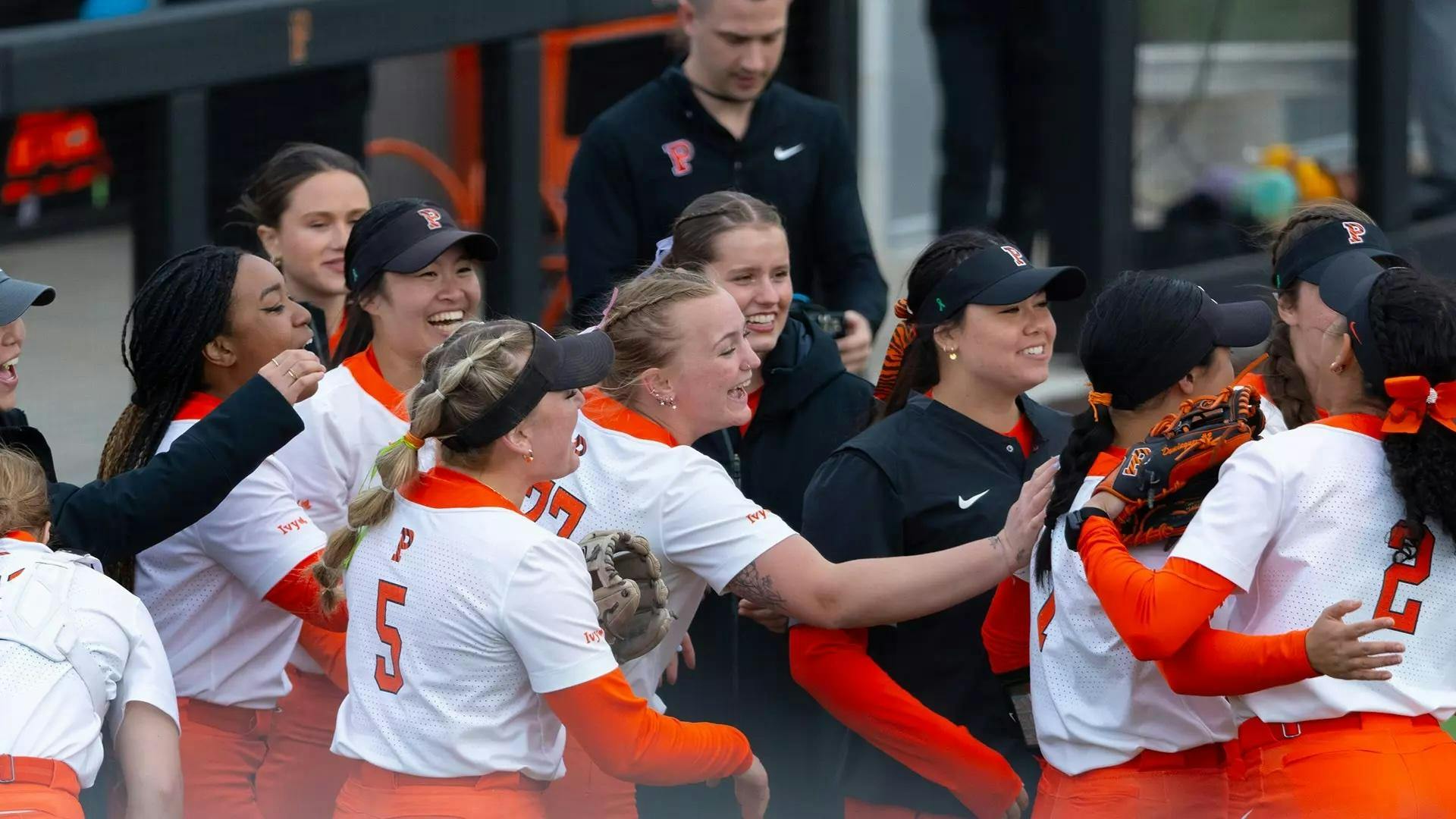Group of softball players smile and celebrate in front of their dugout.