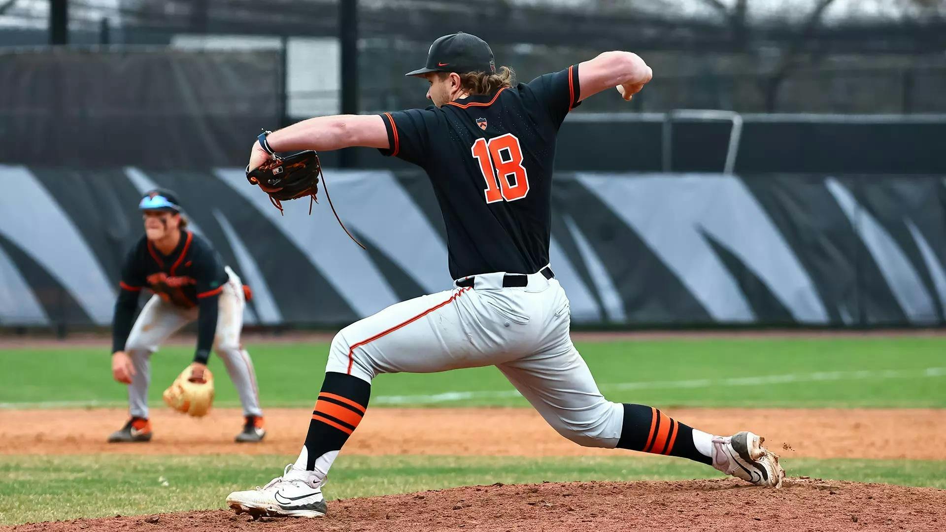 Pitcher in a black Princeton lunges as he throws a pitch from the pitchers mound.