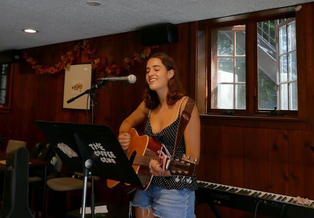 Woman dressed in black and white sings and plays guitar in a café.