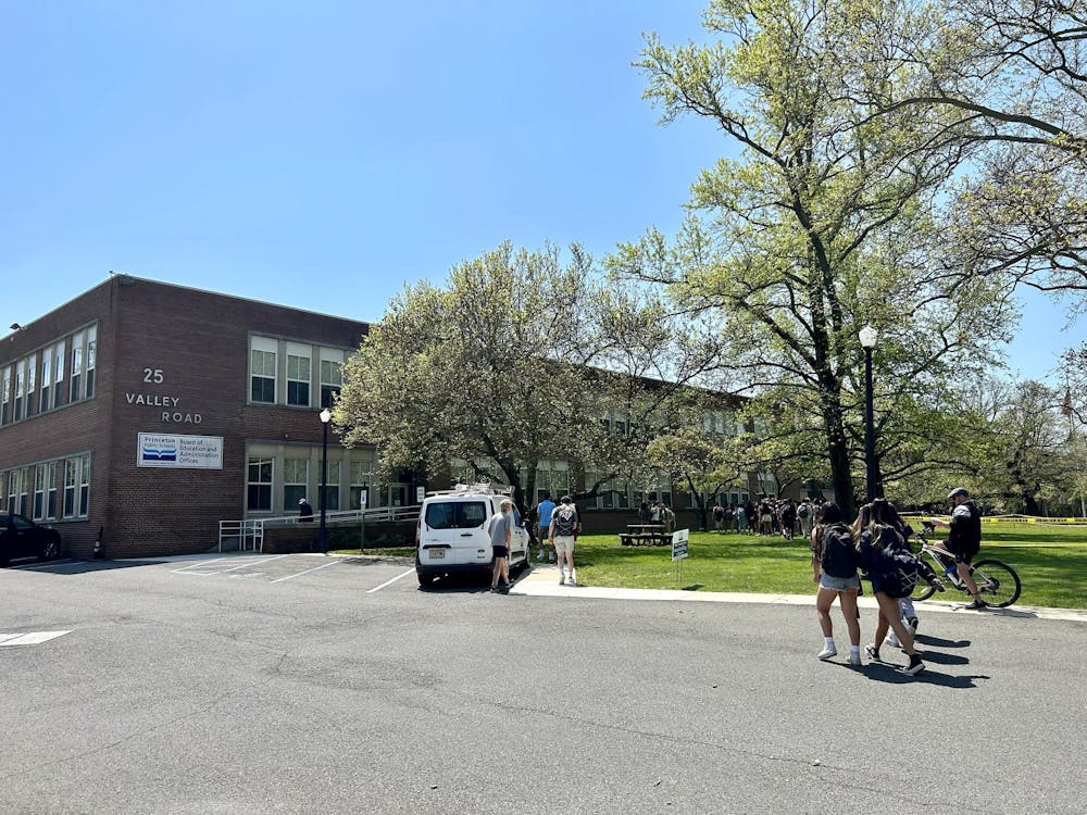 Students wearing backpacks walk across a parking lot toward a brown school building.