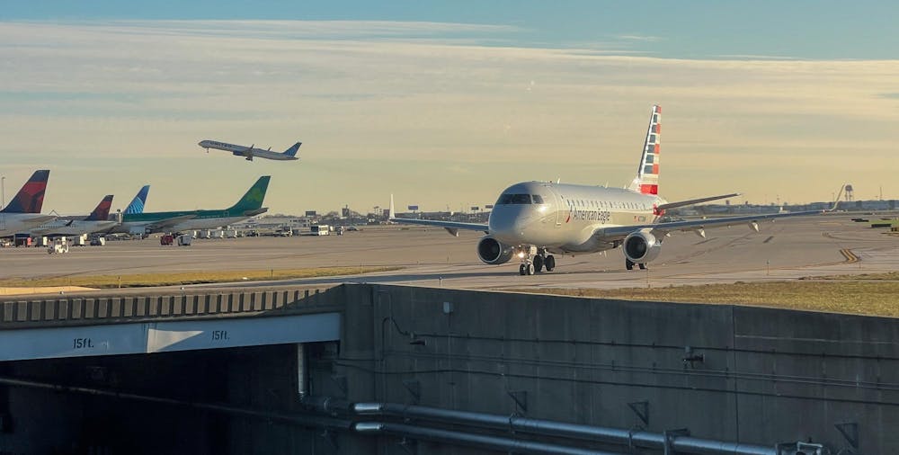 Airplane about to cross a bridge over road. Sky behind the plane is blue streaked with clouds.