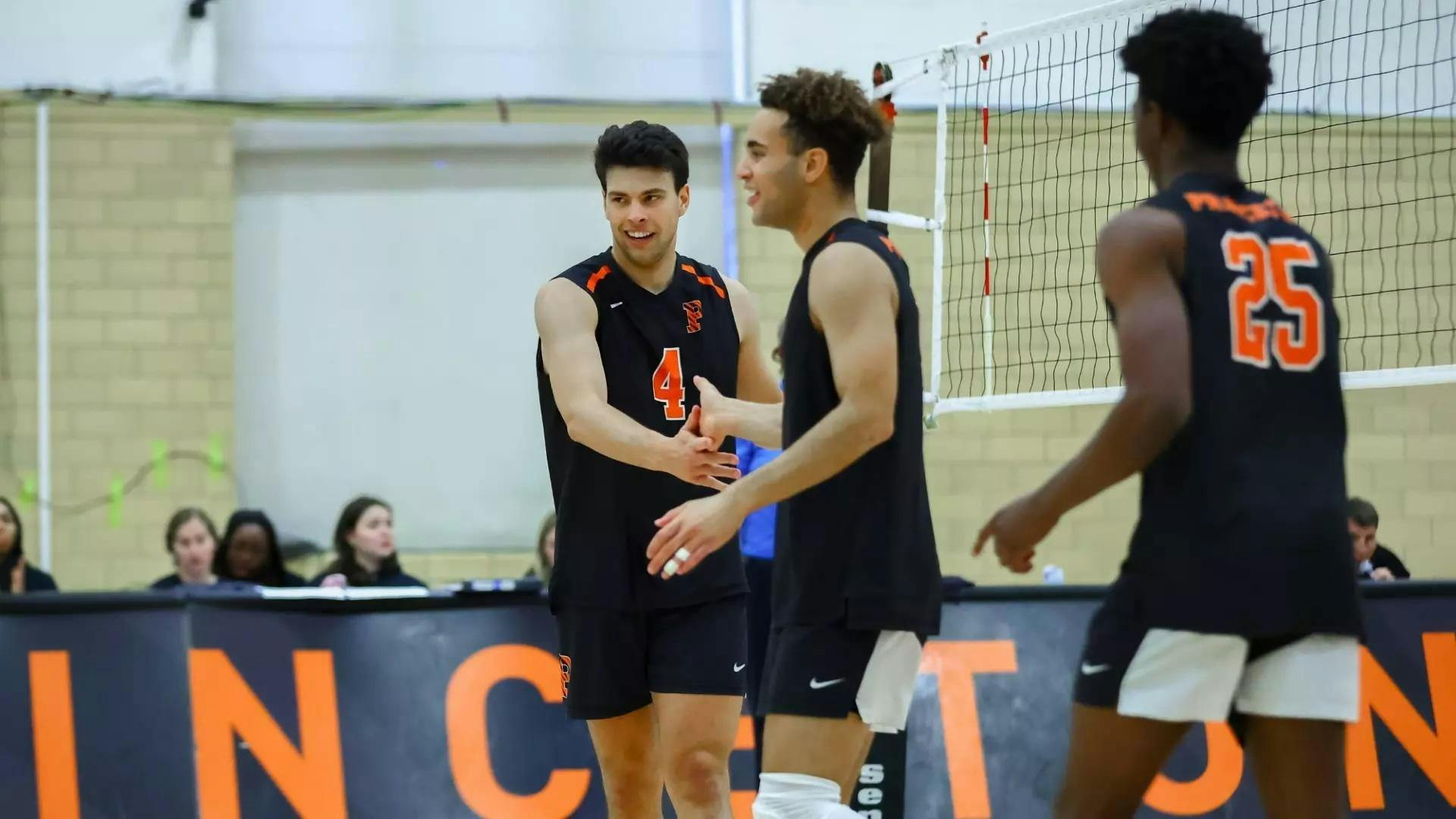 Volleyball players in black uniforms high five on the court.