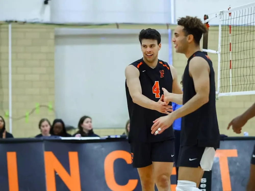 Volleyball players in black uniforms high five on the court.