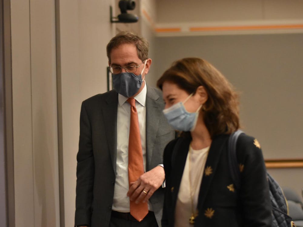 A man wearing a face mask looks down, slightly behind a woman wearing a face mask.