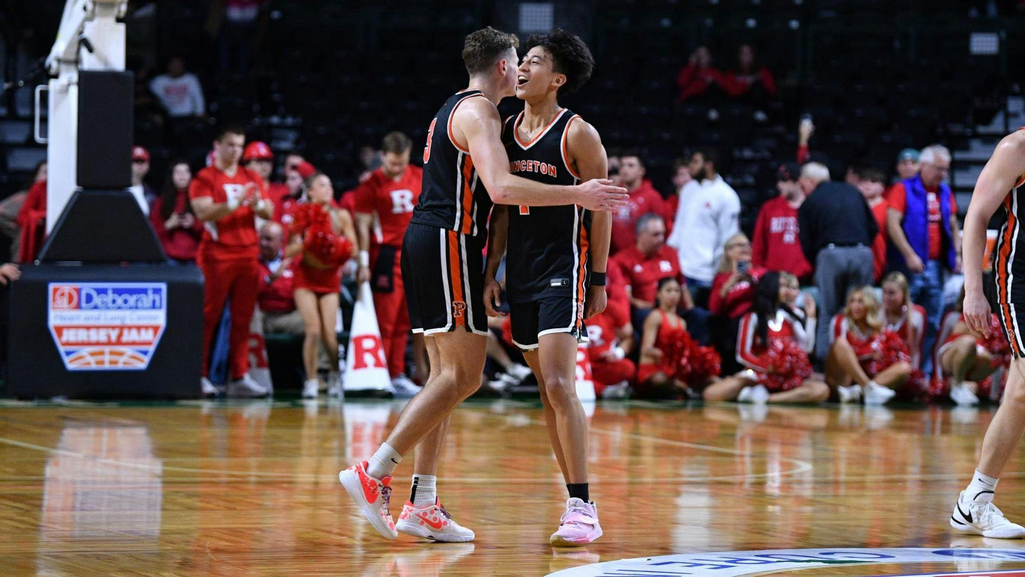 Two basketball players wearing orange and black jerseys embrace on a court.