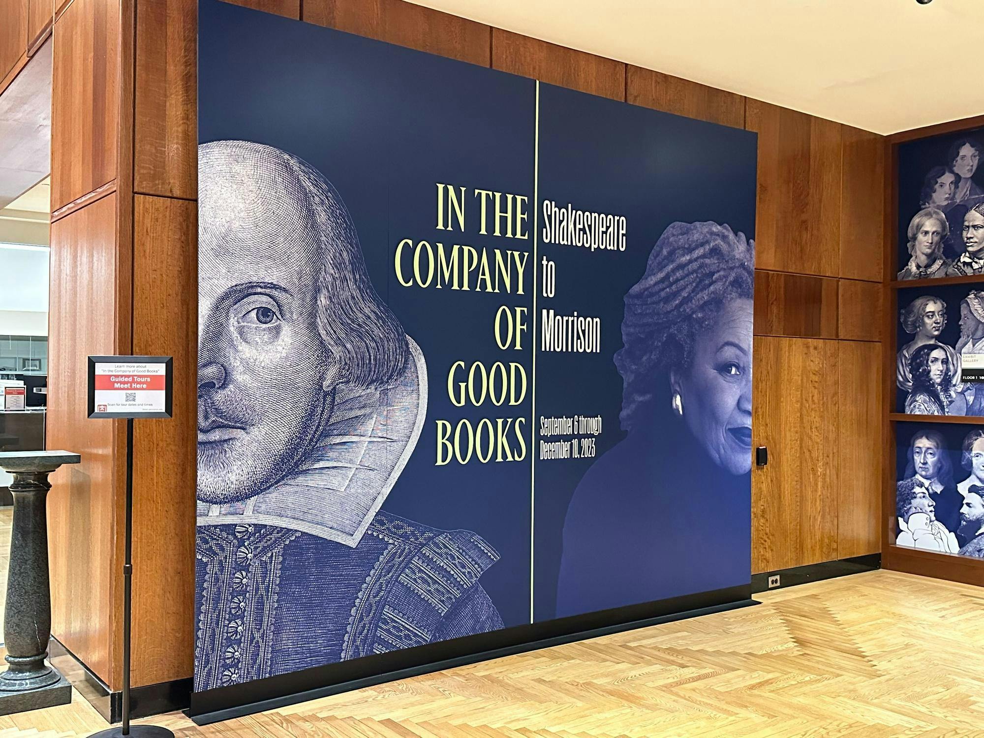 The sign for the exhibition in the first floor of Firestone. The sign is colored navy blue. On the left half is half of Shakespeare's face along with the words "In the Company of Good Books," and the right shows half of Toni Morrison's face with the words "Shakespeare to Morrison: September 6 through December 10, 2023." 